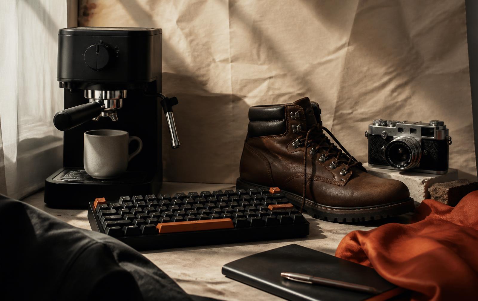 Espresso machine, mechanical keyboard, hiking boot and camera on a paper backdrop
